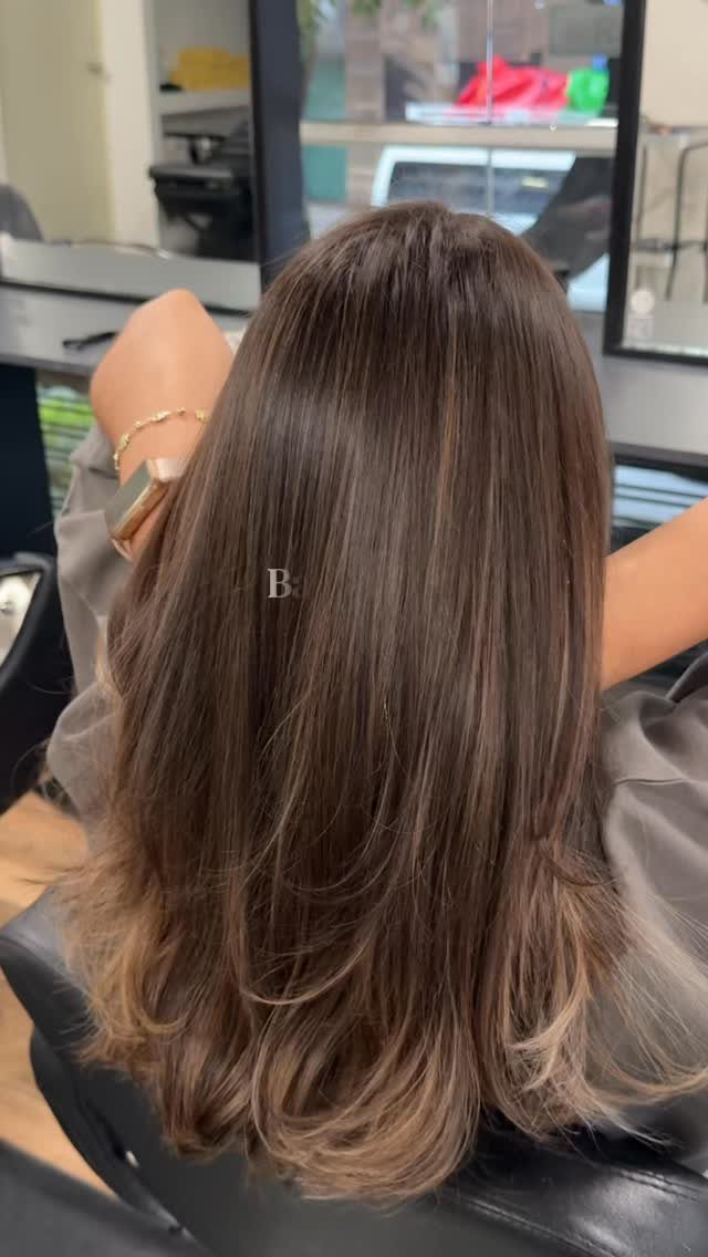 Long brown hair with subtle lighter strands and curled ends in a salon