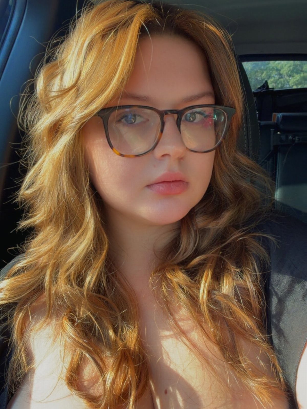 Long wavy light-brown hair with golden highlights frames a person wearing glasses.