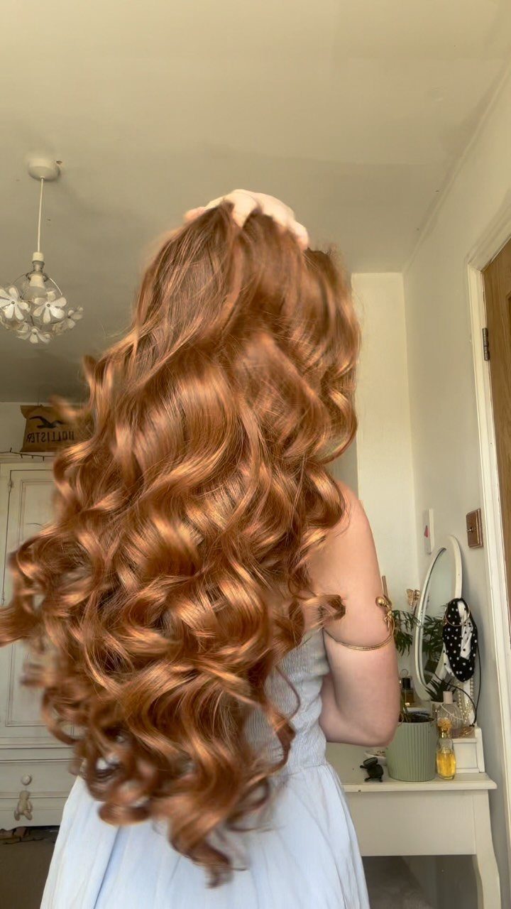 Long auburn-toned curls cascade down the back of a person