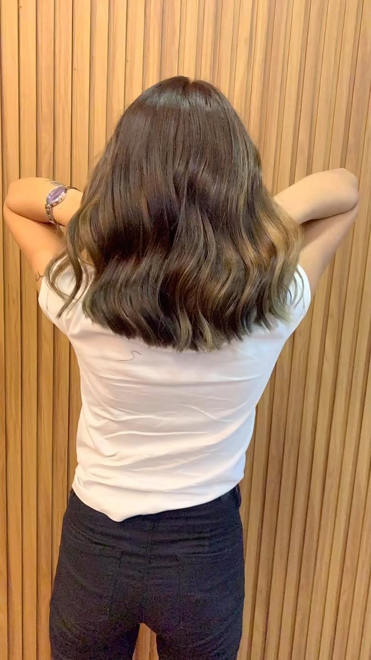 Wavy ash brown hair shown from behind against a wooden panel wall