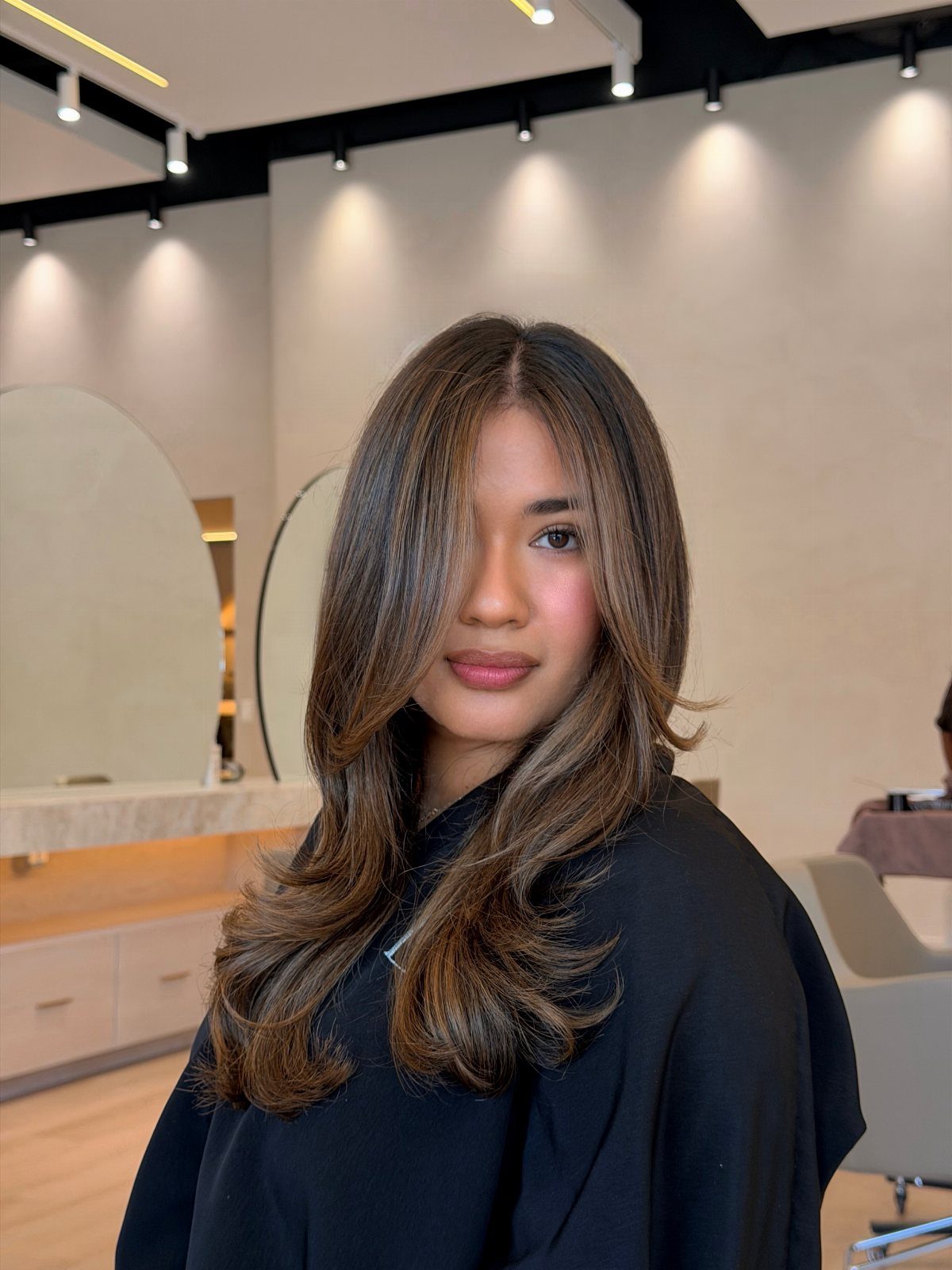 Woman showing long brown hair with lighter blonde highlights in a salon