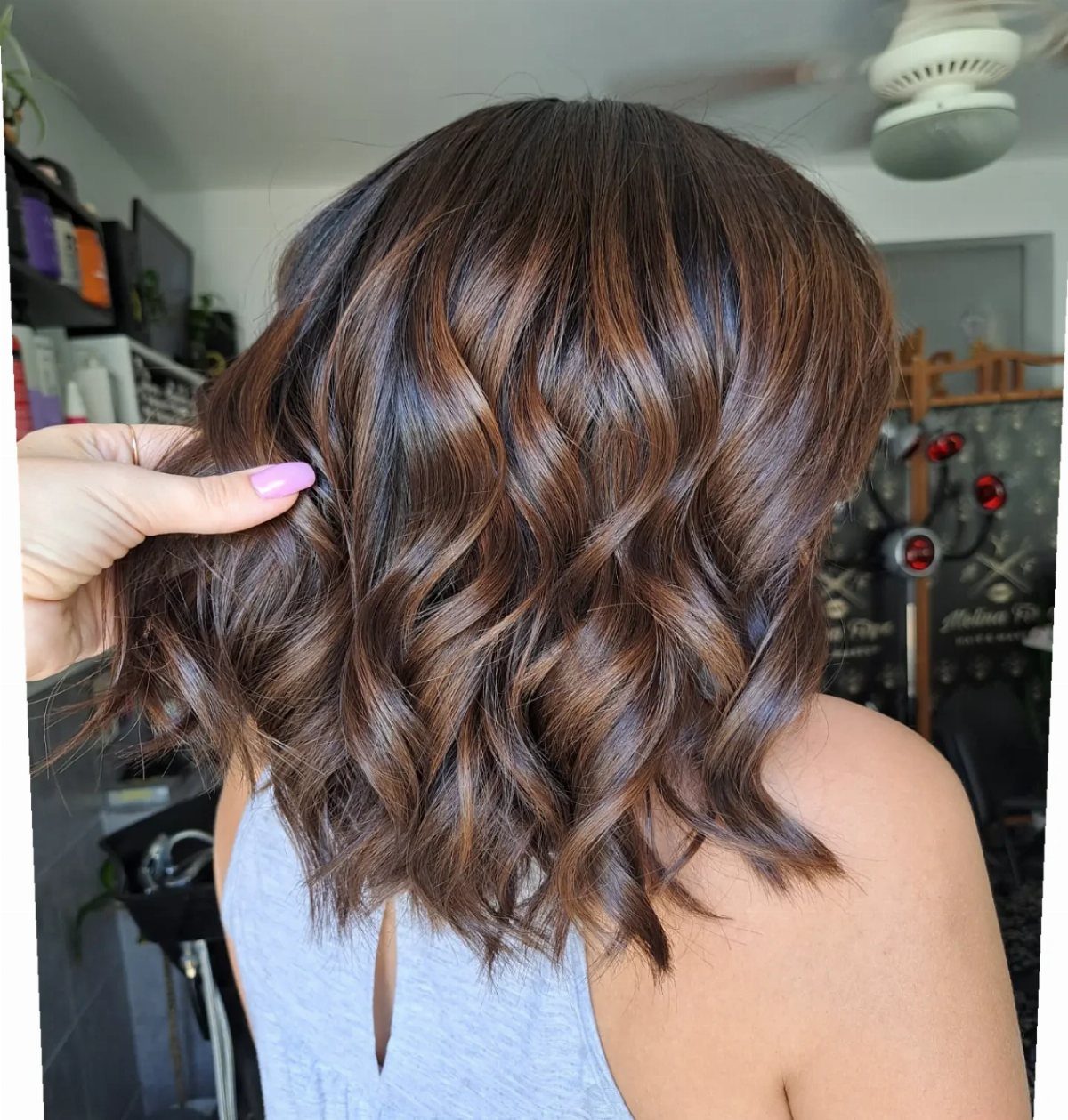 Wavy brunette hair with lighter brown balayage pieces held out by a hand