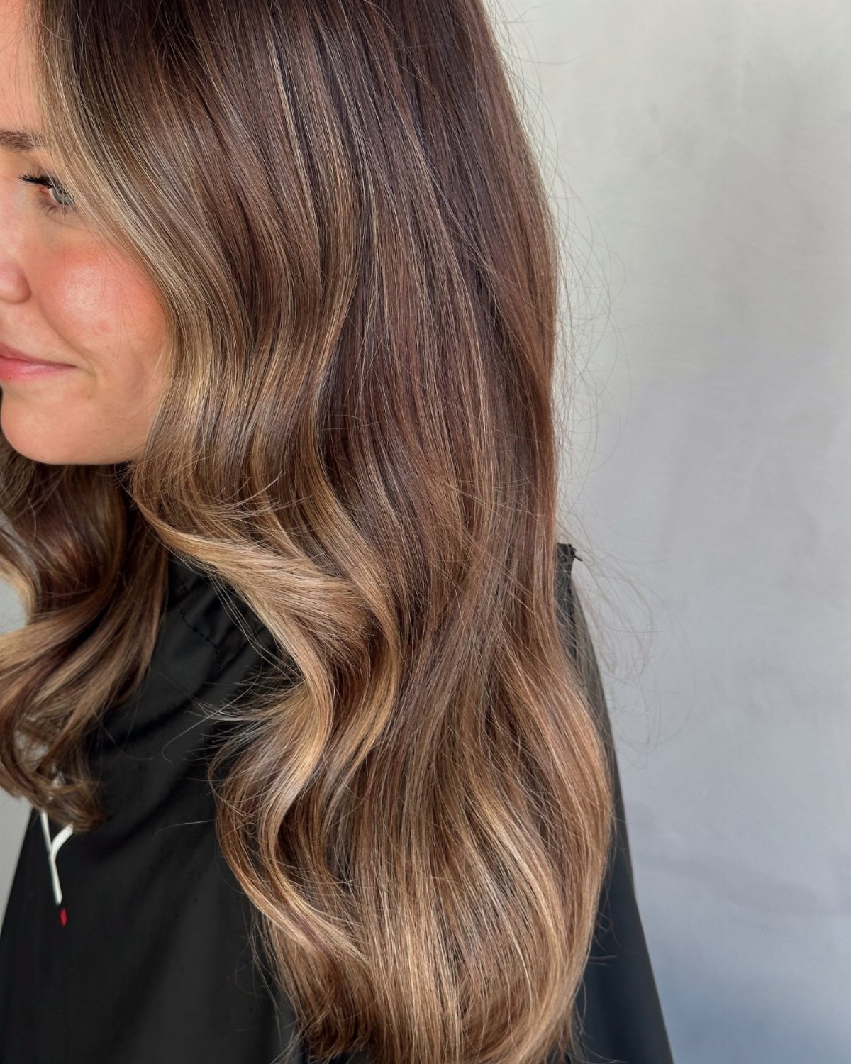 Wavy brown hair with prominent caramel highlights against a light gray background