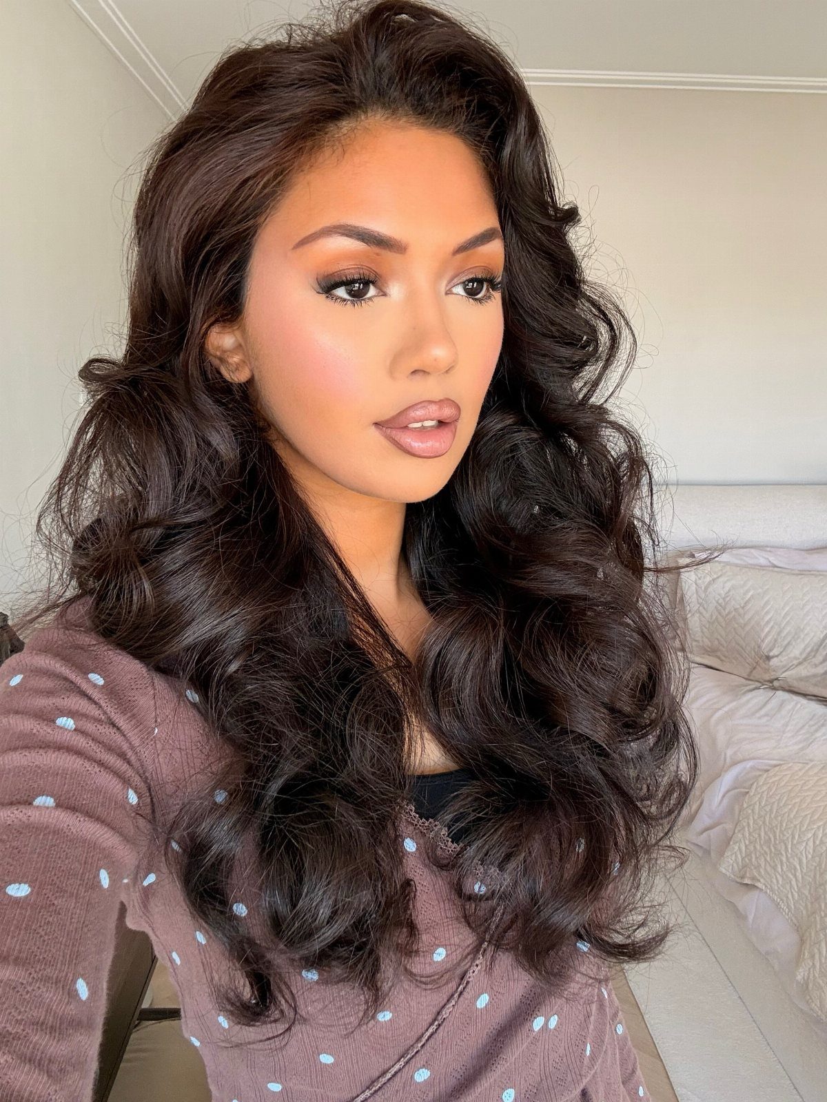 Woman with long, voluminous dark brown waves wearing a mauve polka-dot top