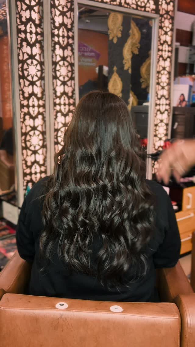 Long, deep brown wavy hair shown from behind in a salon