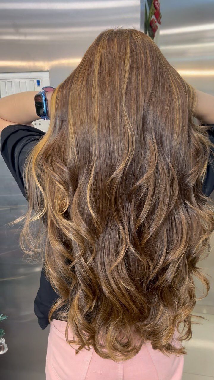 Long golden-brown hair with warm highlights styled in loose curls