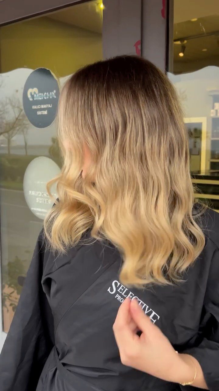 Wavy brown hair fades into honey-toned ends over a black salon cape