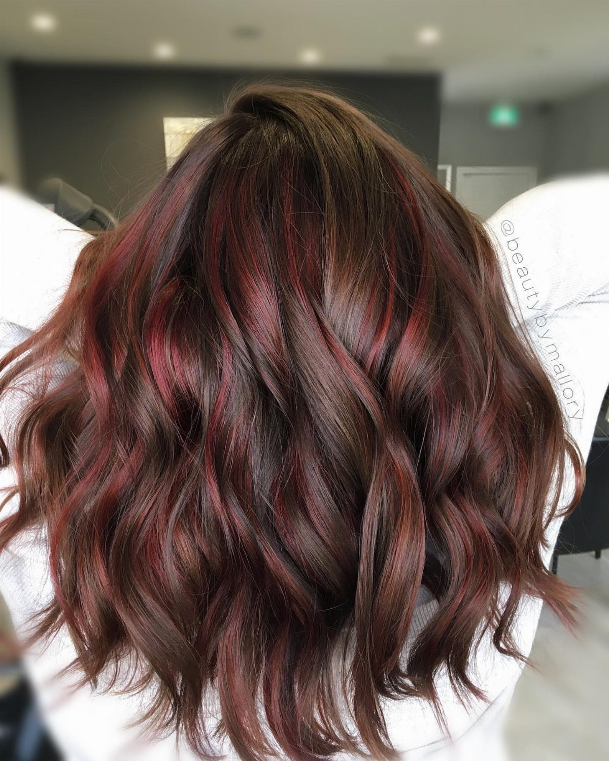 Wavy brown hair with subtle burgundy-red highlights in a salon
