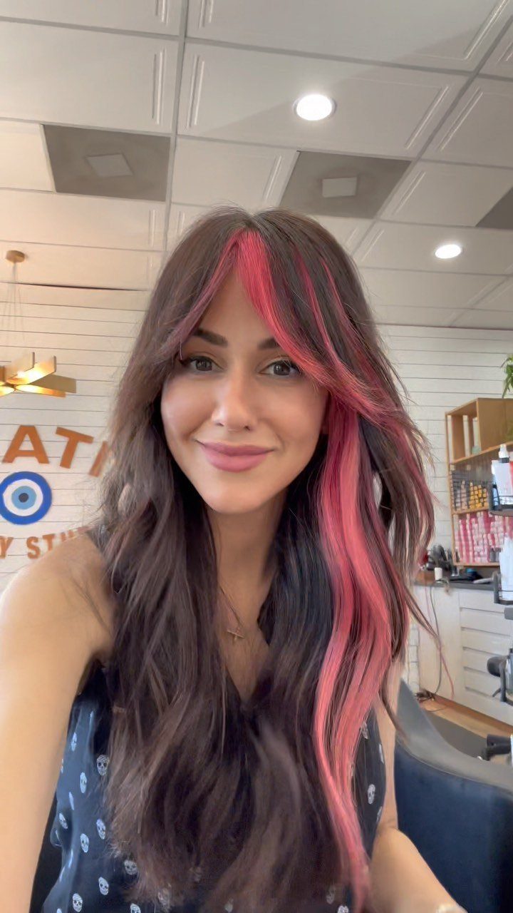 Woman with long dark waves and vivid pink face-framing streaks