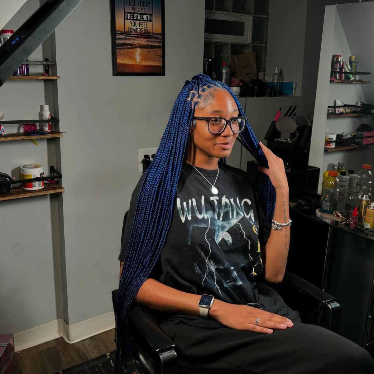 Woman displaying long blue micro braids while seated in a salon chair