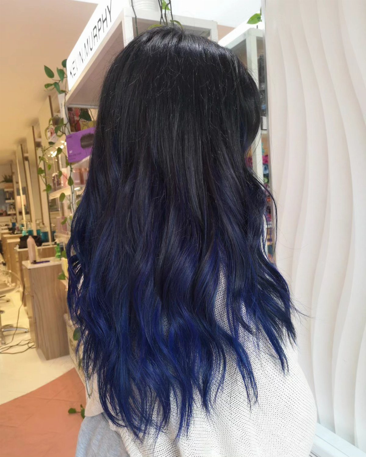 Long wavy hair fades from black roots to deep blue ends in a salon