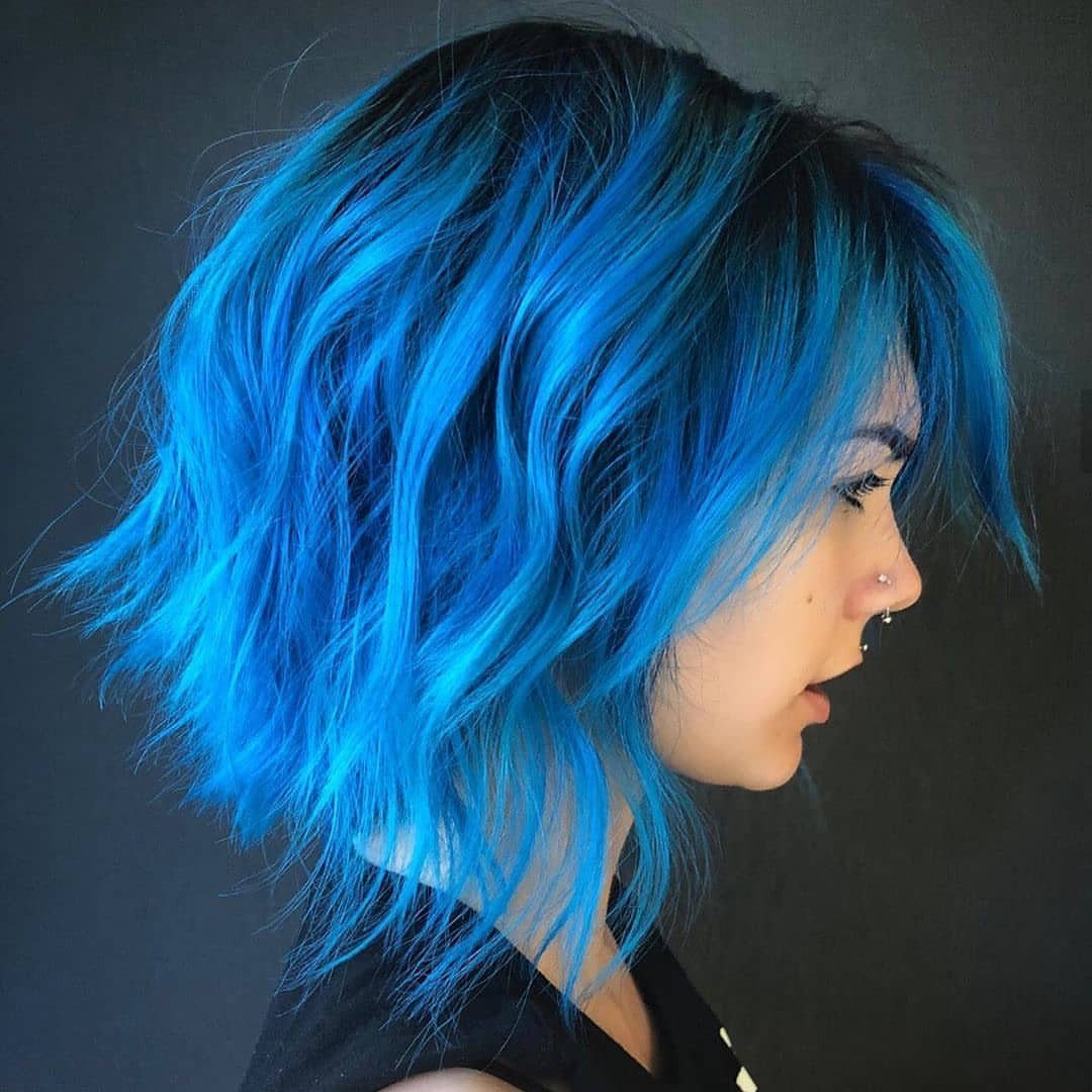 Layered short blue hair with dark roots frames a person's profile