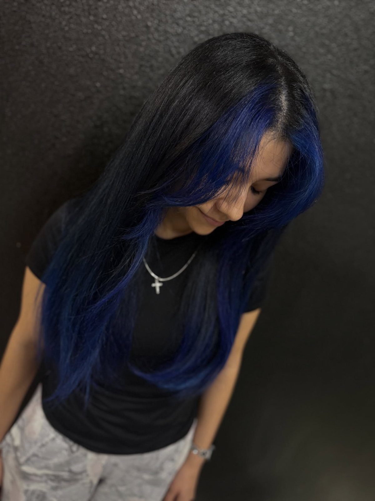 Long dark hair with vivid blue face-framing sections against a dark wall