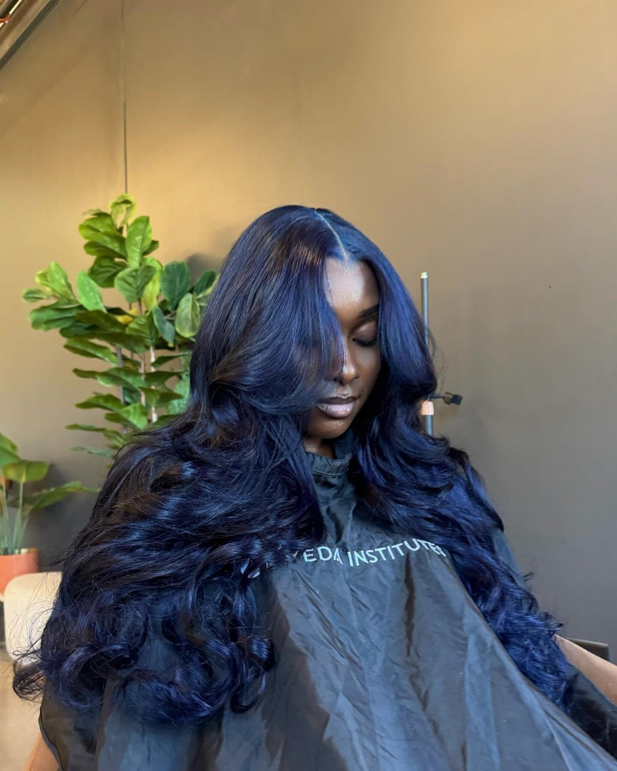 Woman displays long, voluminous blue-black hair with loose curls in a salon