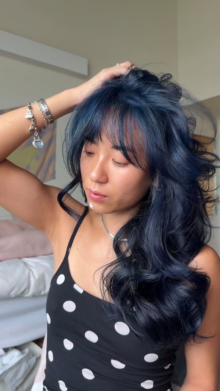 Woman showing long, glossy midnight-blue waves and side-swept bangs