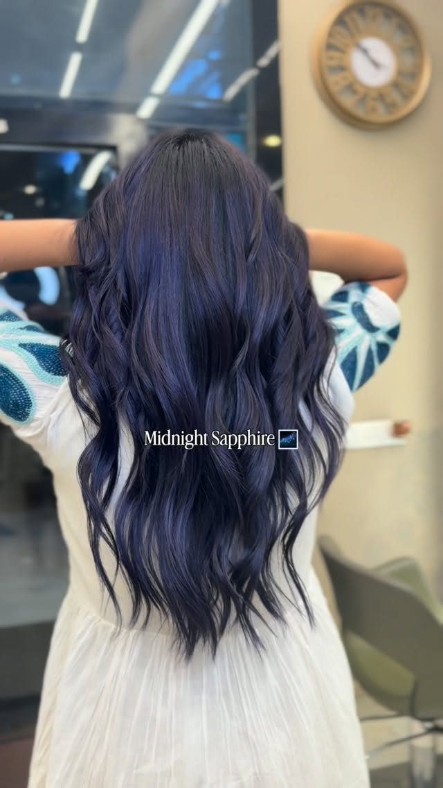 Long wavy dark sapphire-blue hair displayed over a white salon cape