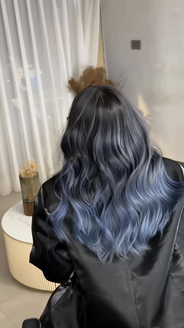 Long wavy smoky grey-blue balayage hair over a black salon cape
