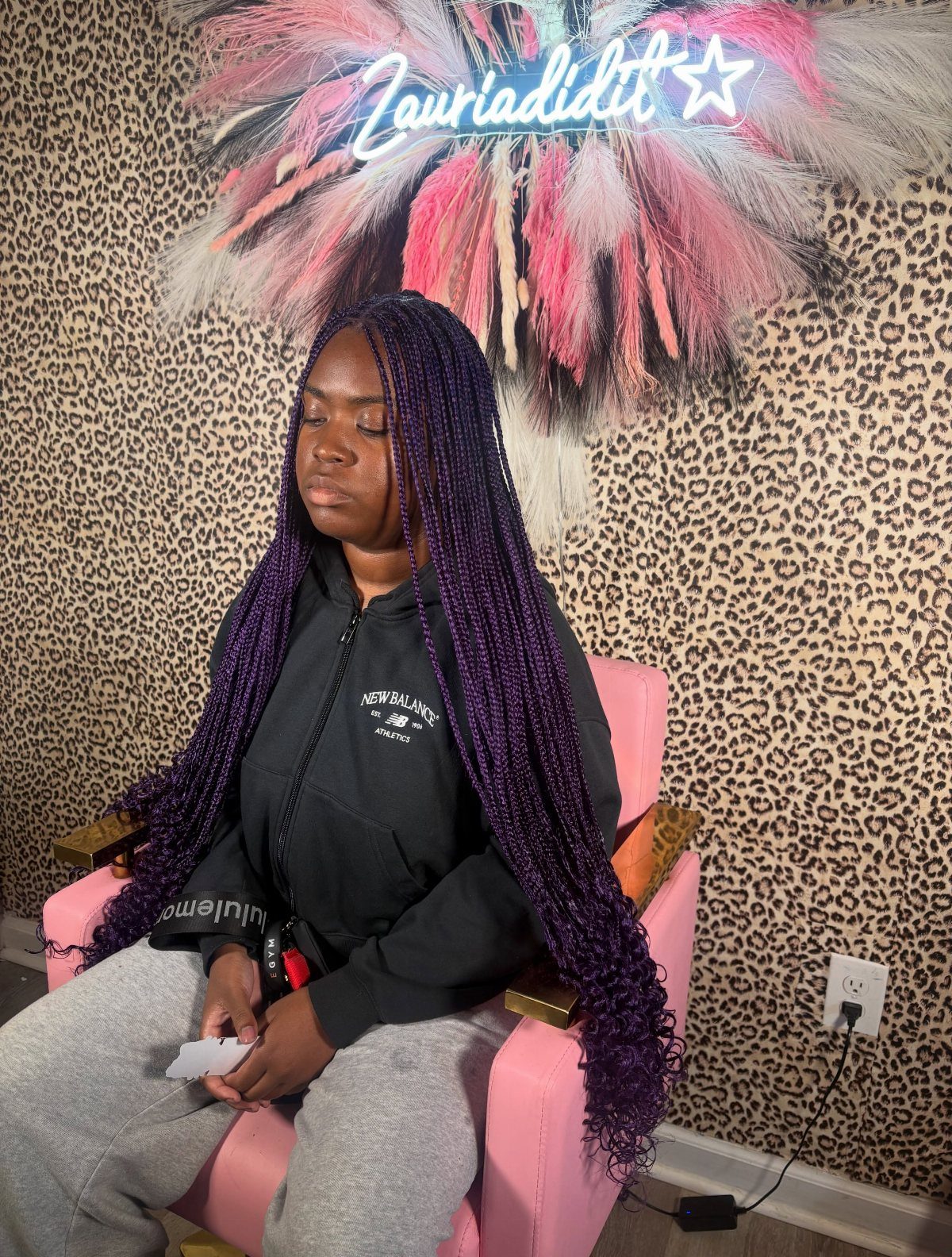Woman with long dark purple braids and curled ends seated in a pink chair