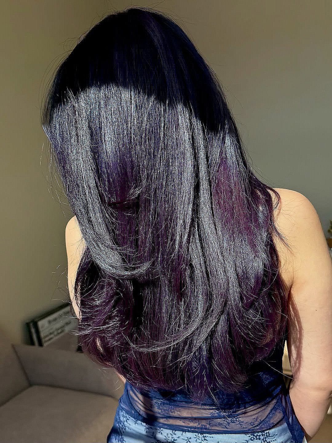 Long midnight-purple hair falls in glossy layers down the person's back.