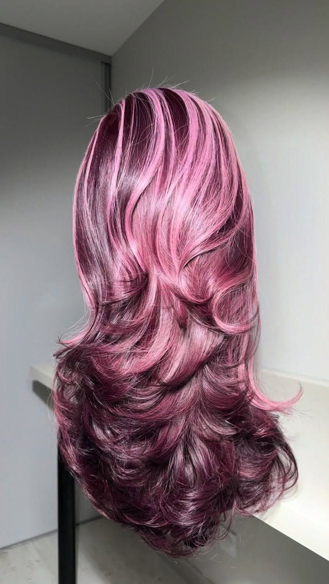 Layered burgundy-purple hair with bright streaks and outward-flipped feathered ends