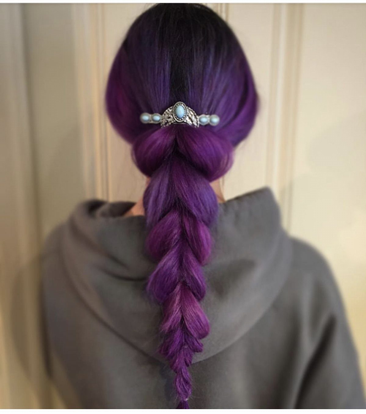 Deep-purple hair gathered into a loose low braid with a jeweled clip