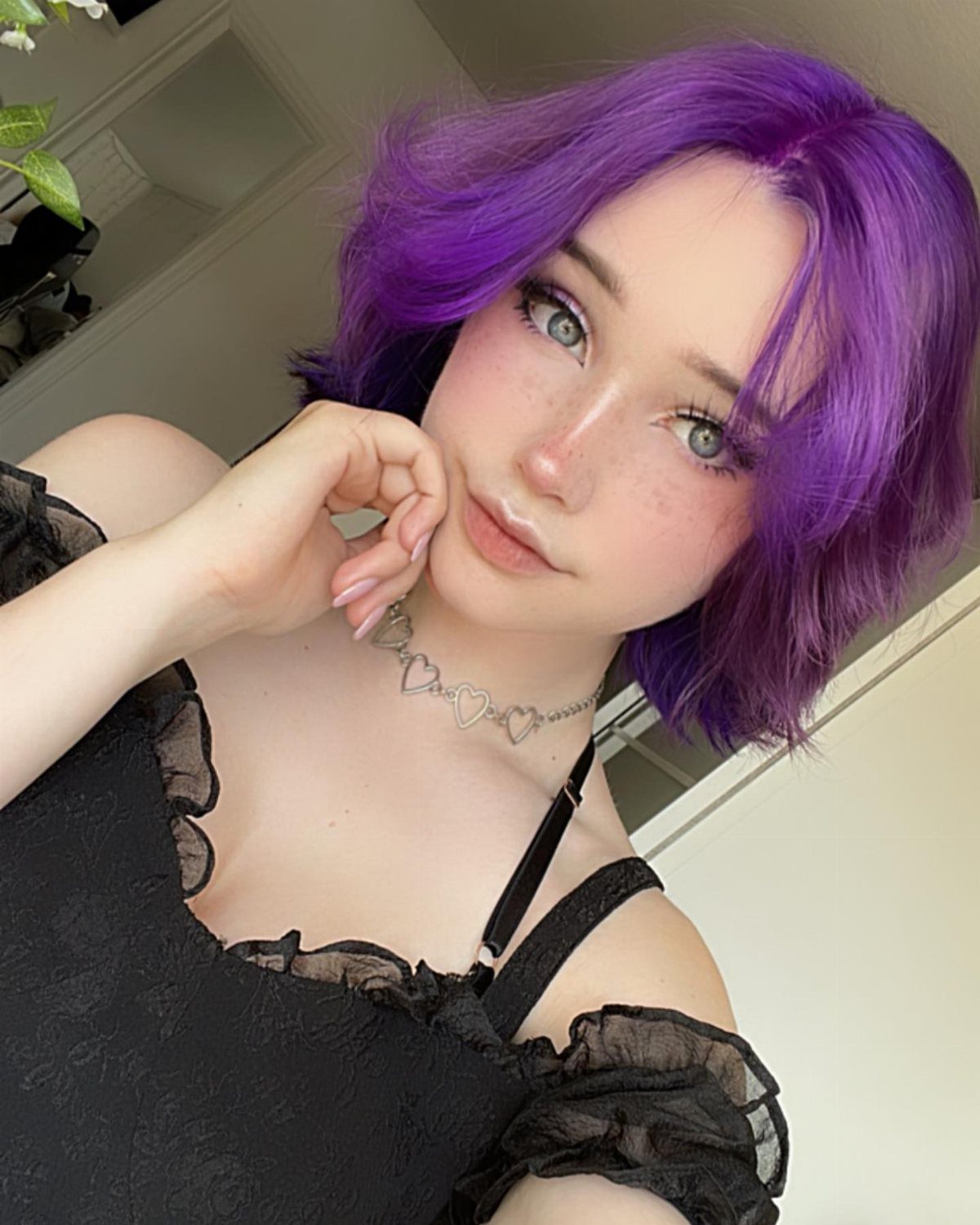 Person with short vivid purple hair and a side part posing indoors