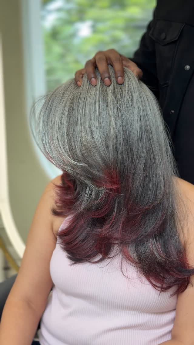Layered grey hair with burgundy-red ends styled on a seated salon client