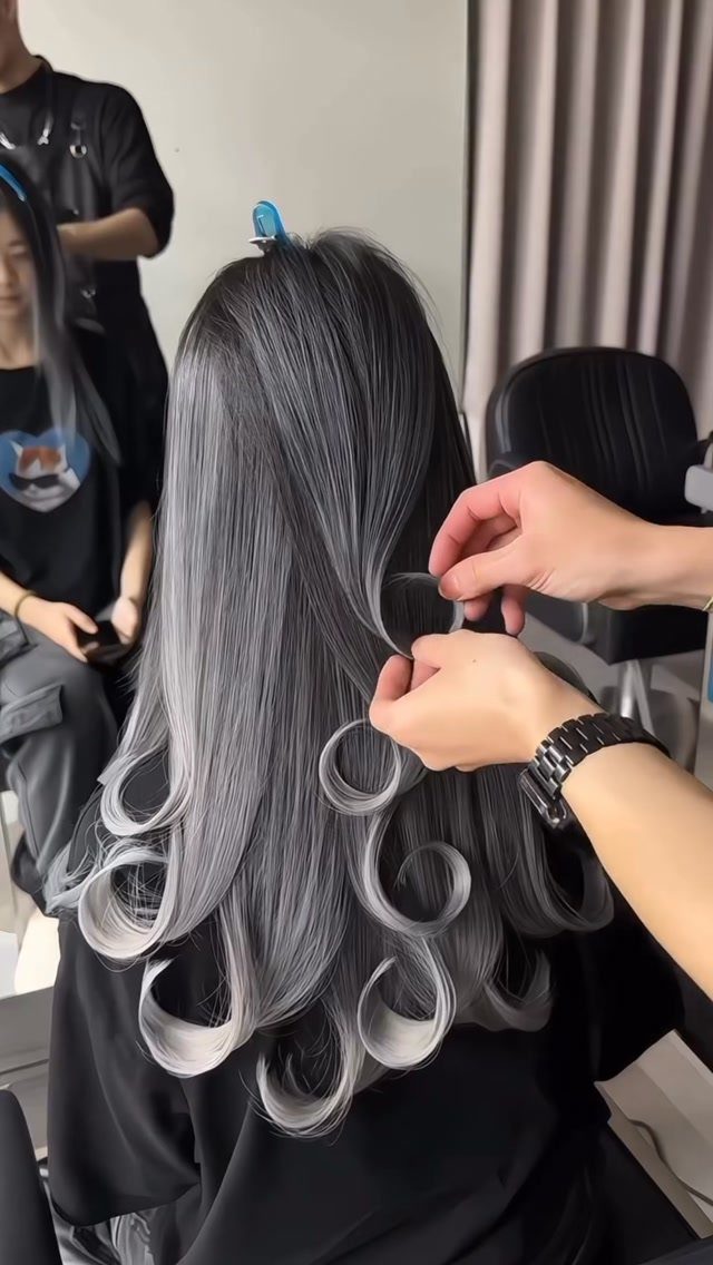 Long silver-grey dyed hair styled in glossy curls at a salon