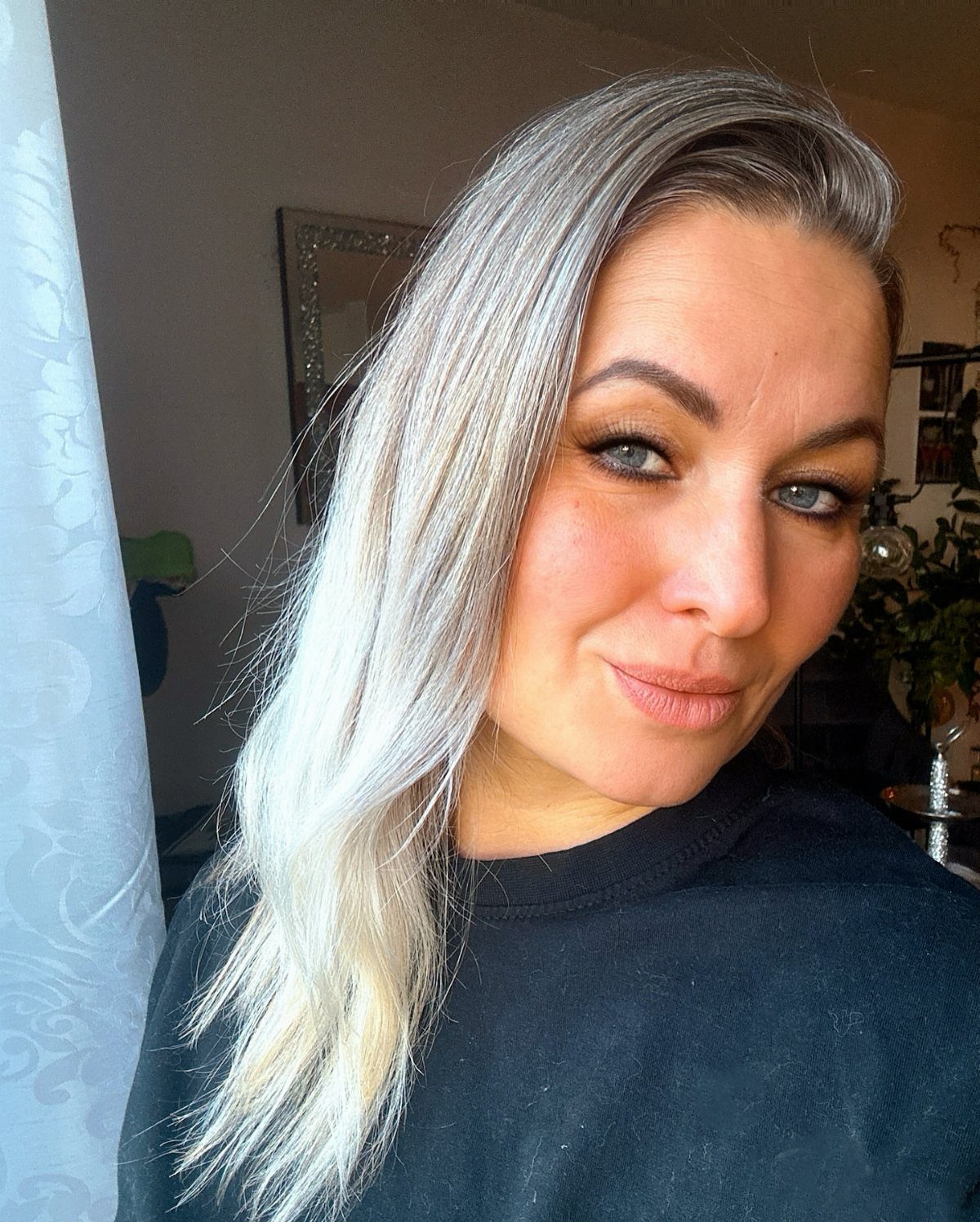 Woman with long, cool silver-blonde hair and darker roots poses indoors
