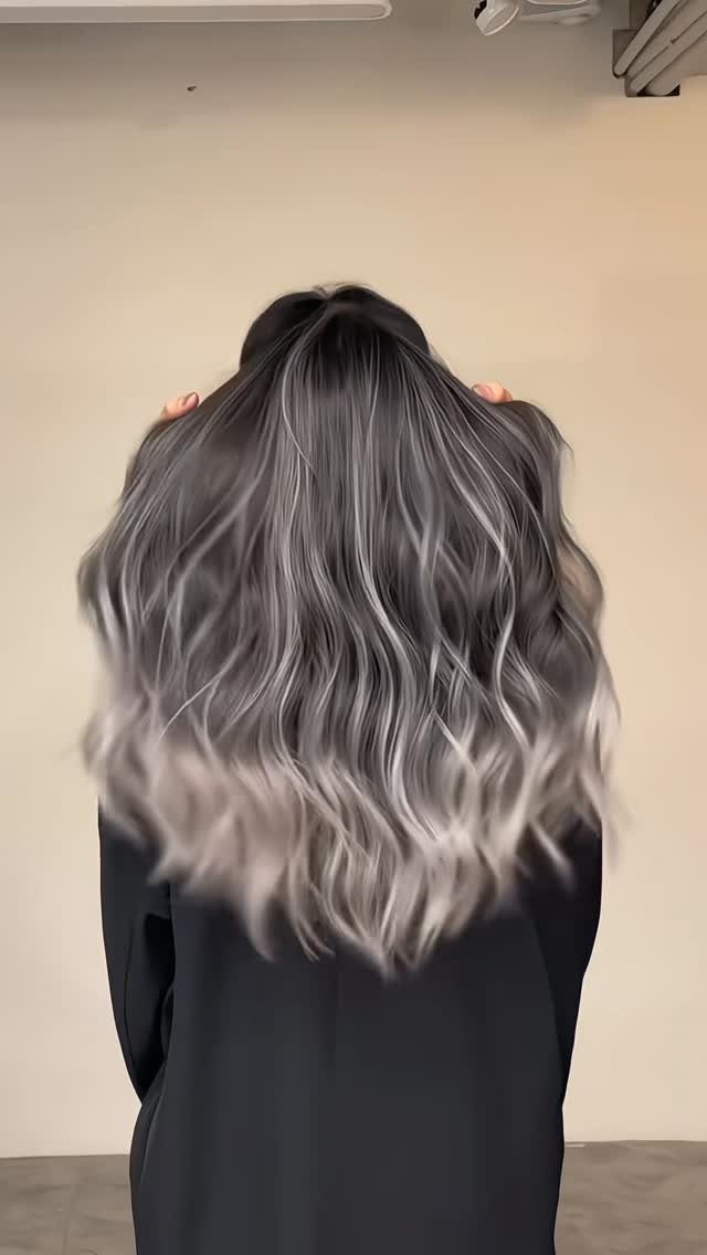 Long wavy dark hair transitions into smoky silver-gray balayage with pale ash ends