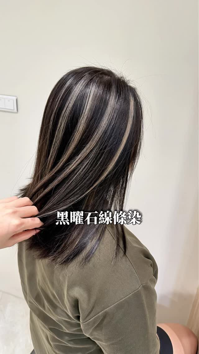 Dark wavy hair with distinct silver-gray ribbons held out by a hand