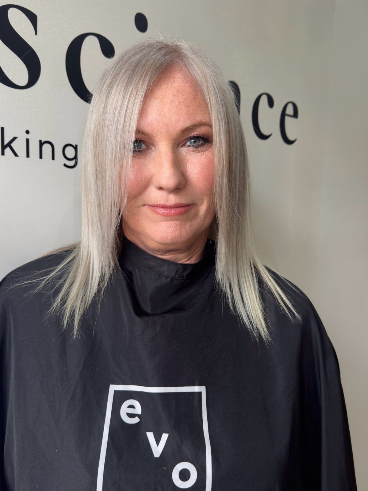 Woman with long, straight silver hair posing in a black salon cape