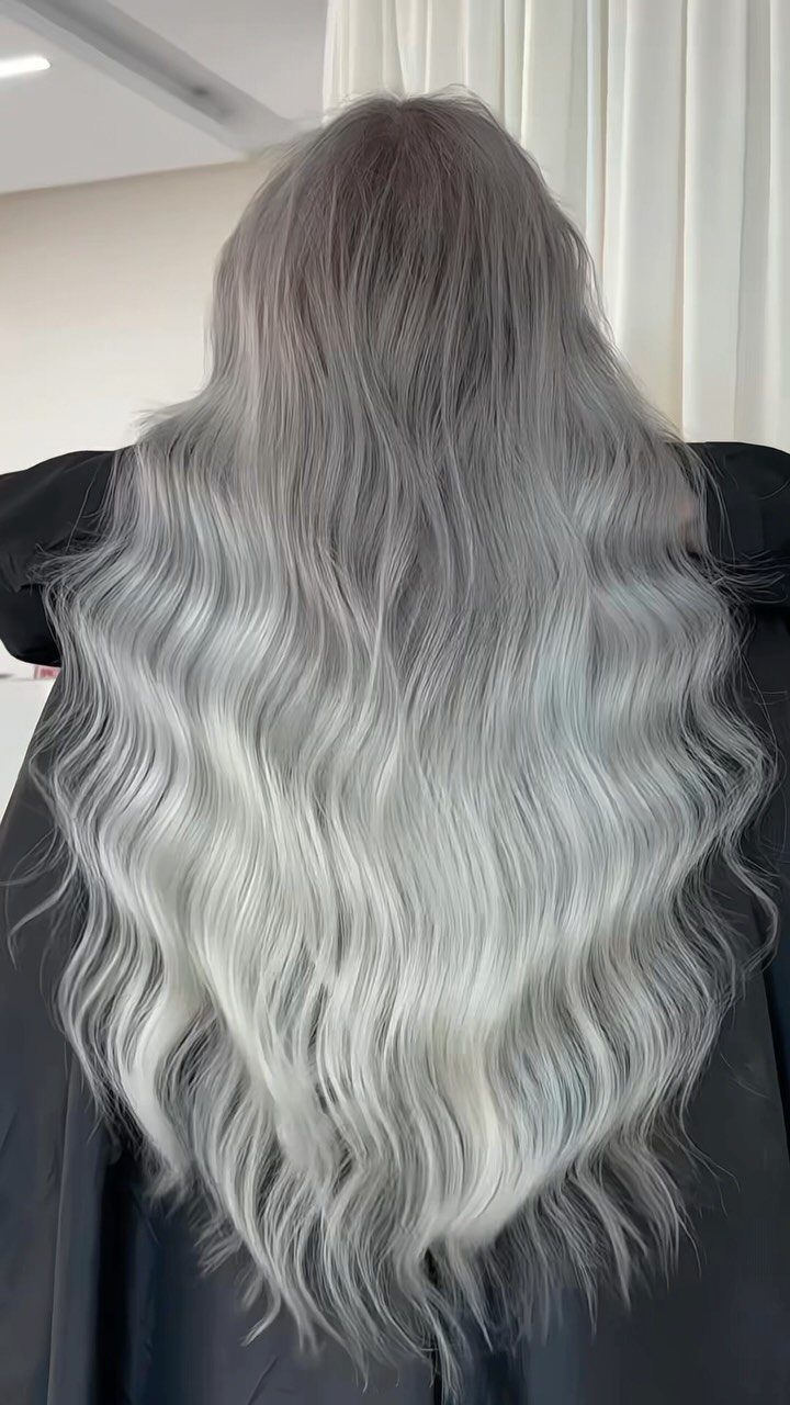 Long silver-gray waves with dark roots drape over a black salon cape