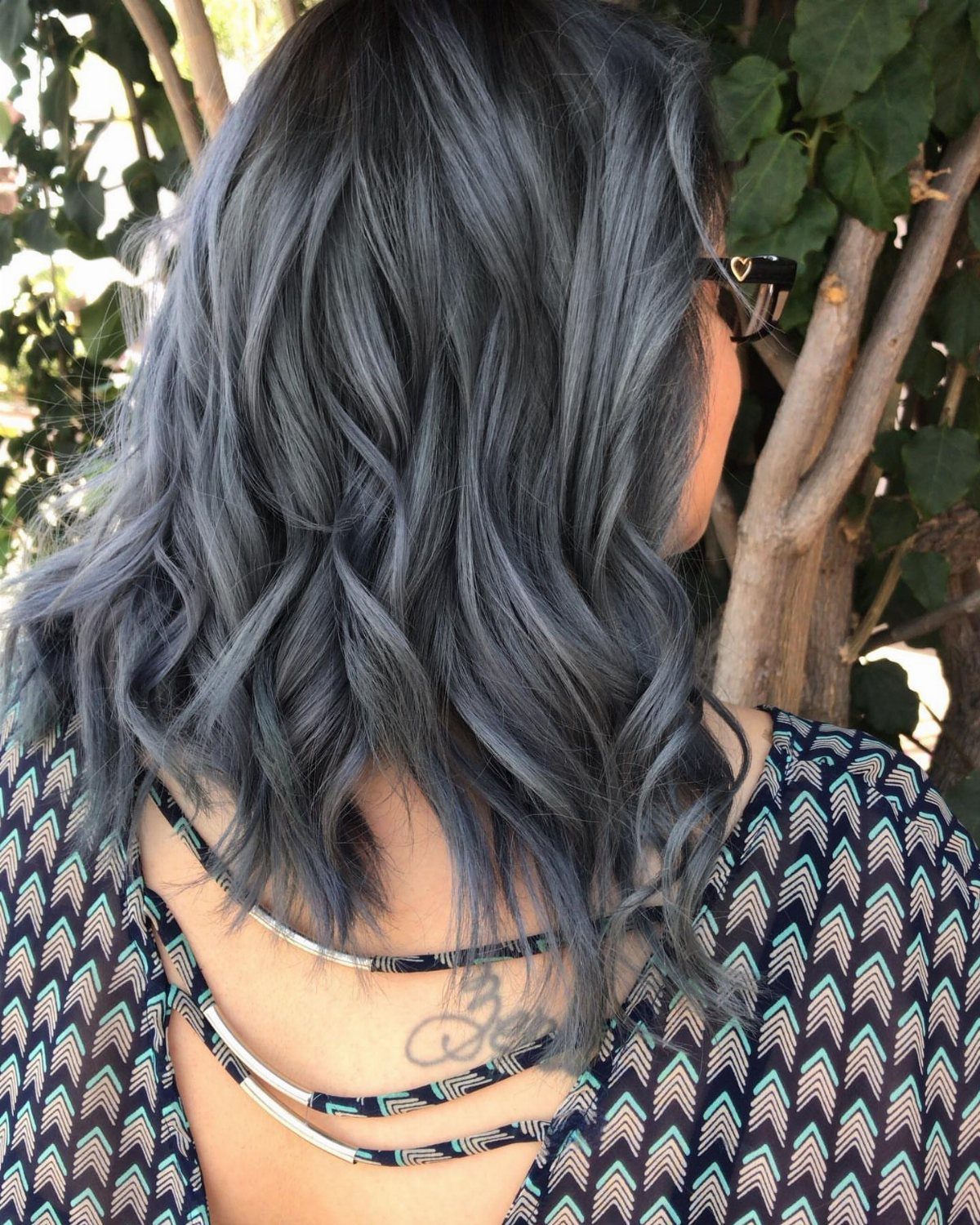 Long wavy charcoal-gray hair photographed from behind beside a tree