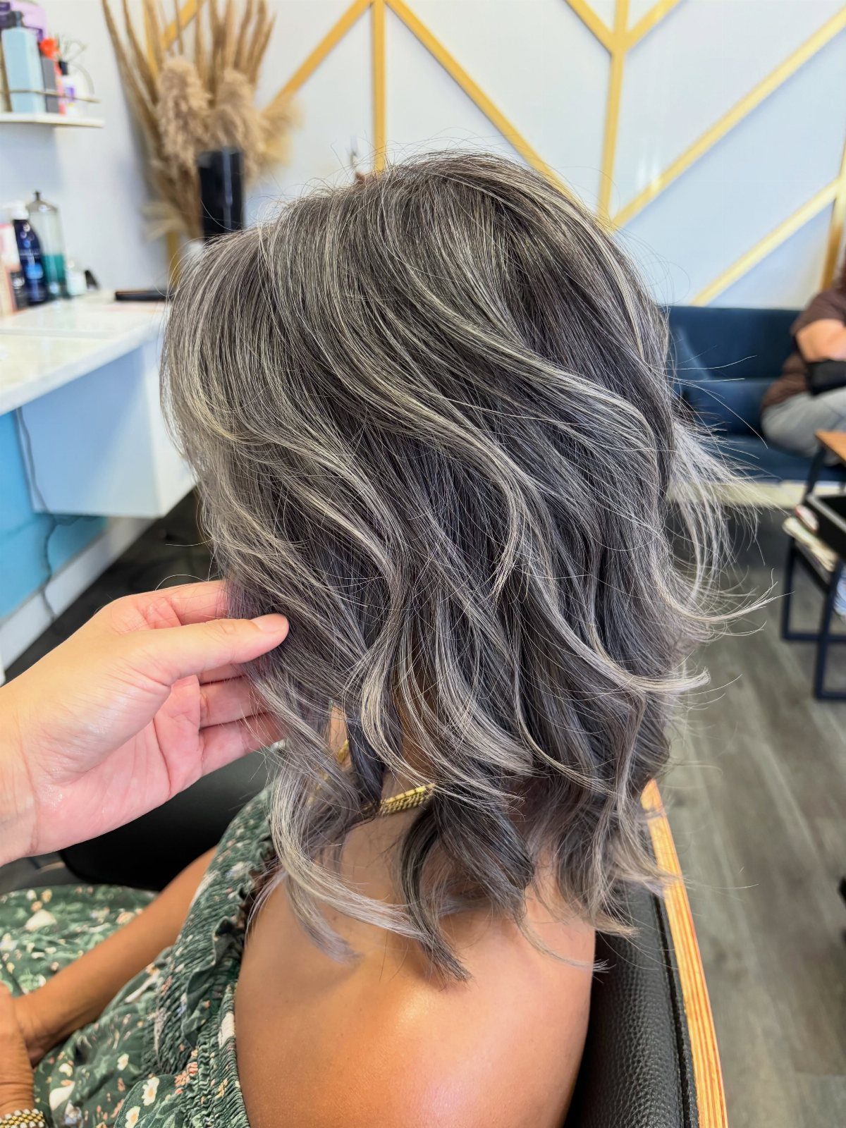 Wavy charcoal and silver balayage hair with dark roots in a salon