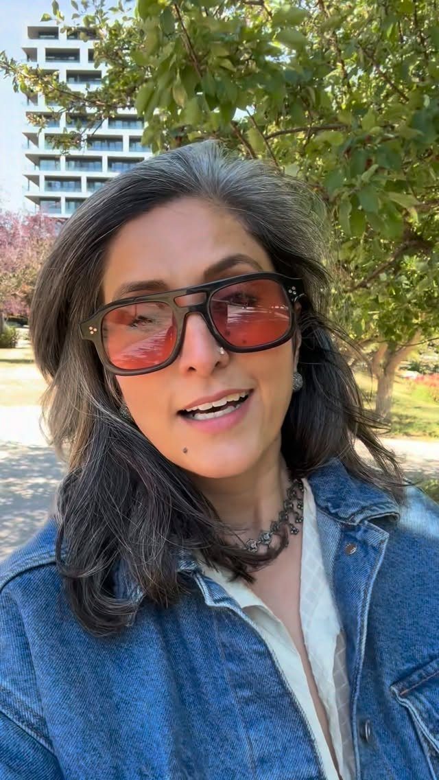 Woman with long dark hair and gray streaks wearing sunglasses and a denim jacket
