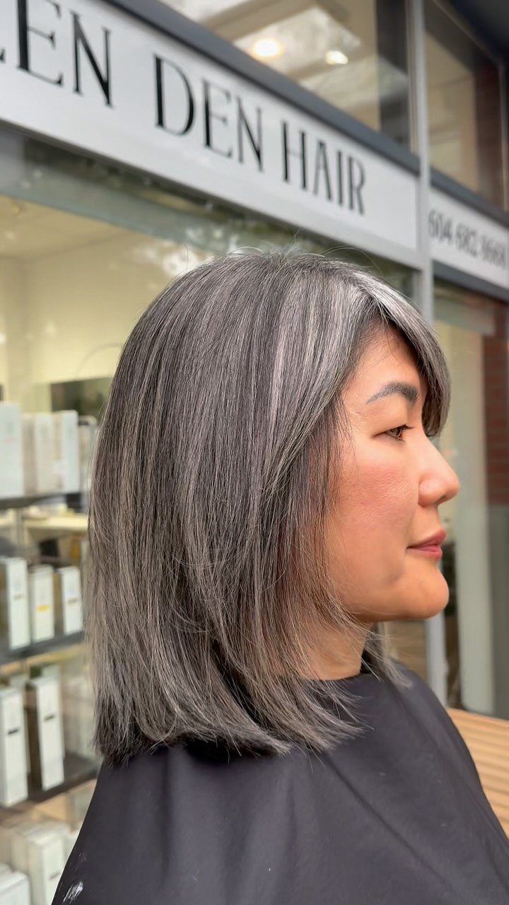Woman with straight gray hair stands in profile outside a hair salon
