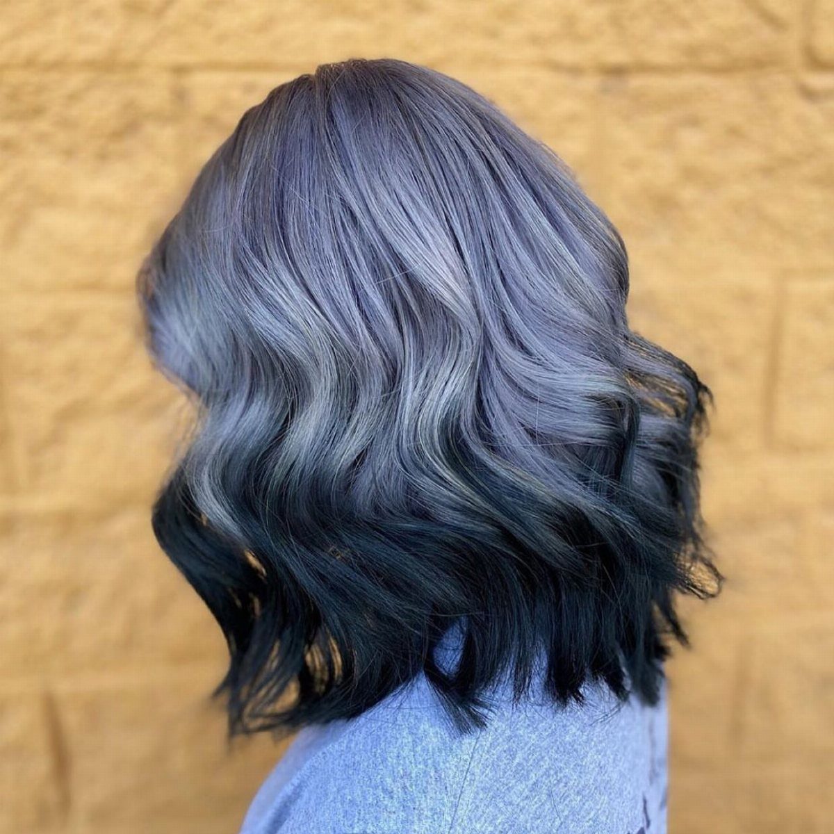 Wavy gray-lavender bob fading into dark charcoal ends against a tan brick wall
