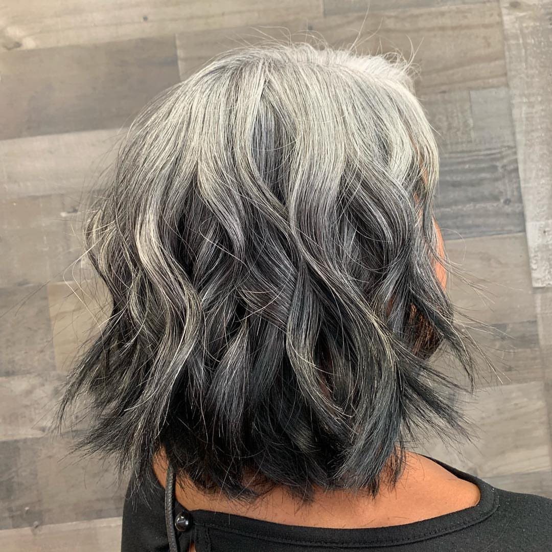 Wavy silver-gray hair transitions into dark charcoal ends against a tiled wall.