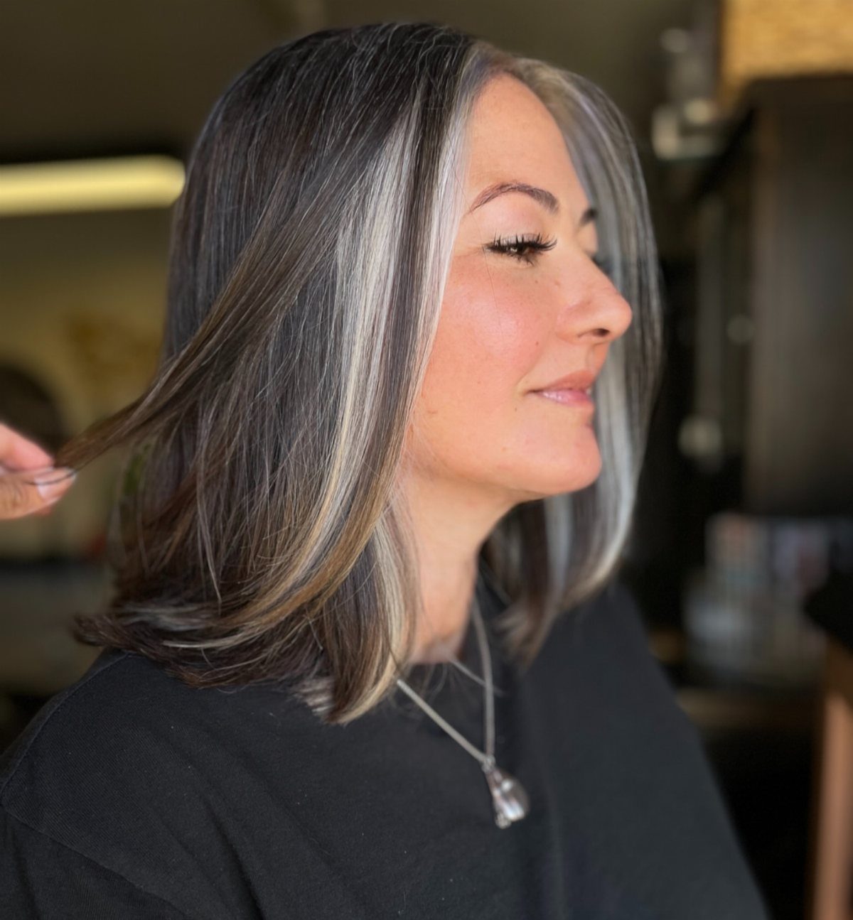 Woman with dark gray hair and bold silver-white face-framing color accents