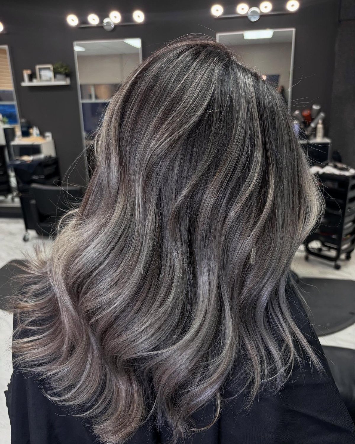 Wavy slate gray hair with soft silver balayage blending in a salon