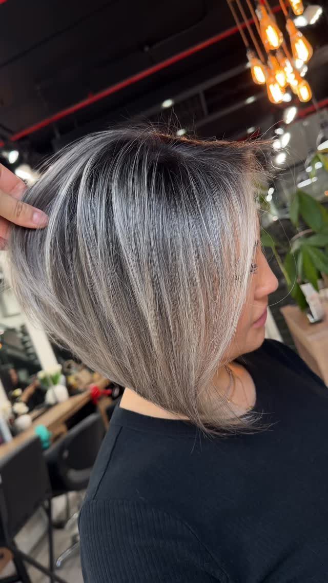 Angled bob with dark roots blended into silver-gray highlights in a salon