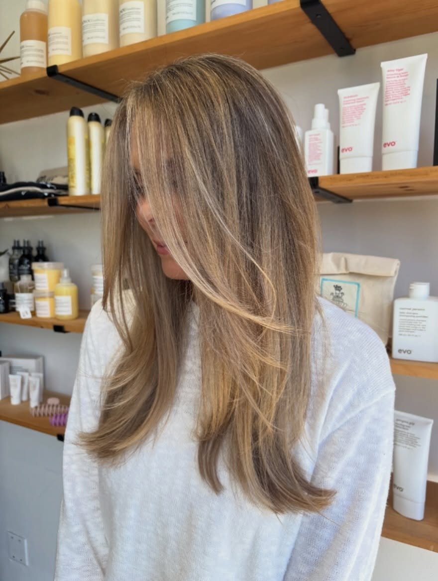 Layered brunette hair with natural-looking blonde balayage highlights in a salon