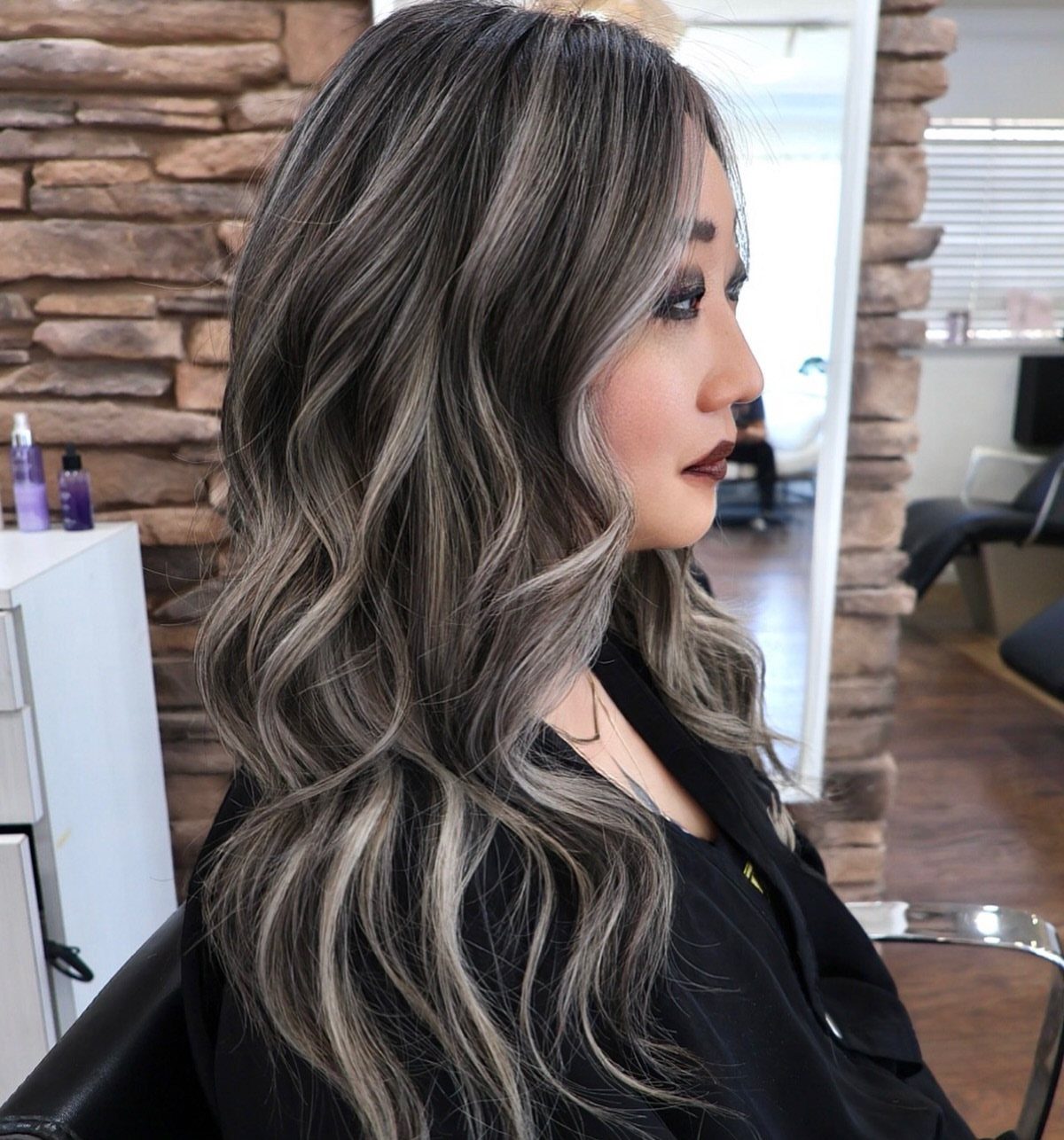 Long dark waves with bold silver-gray highlights styled in a salon