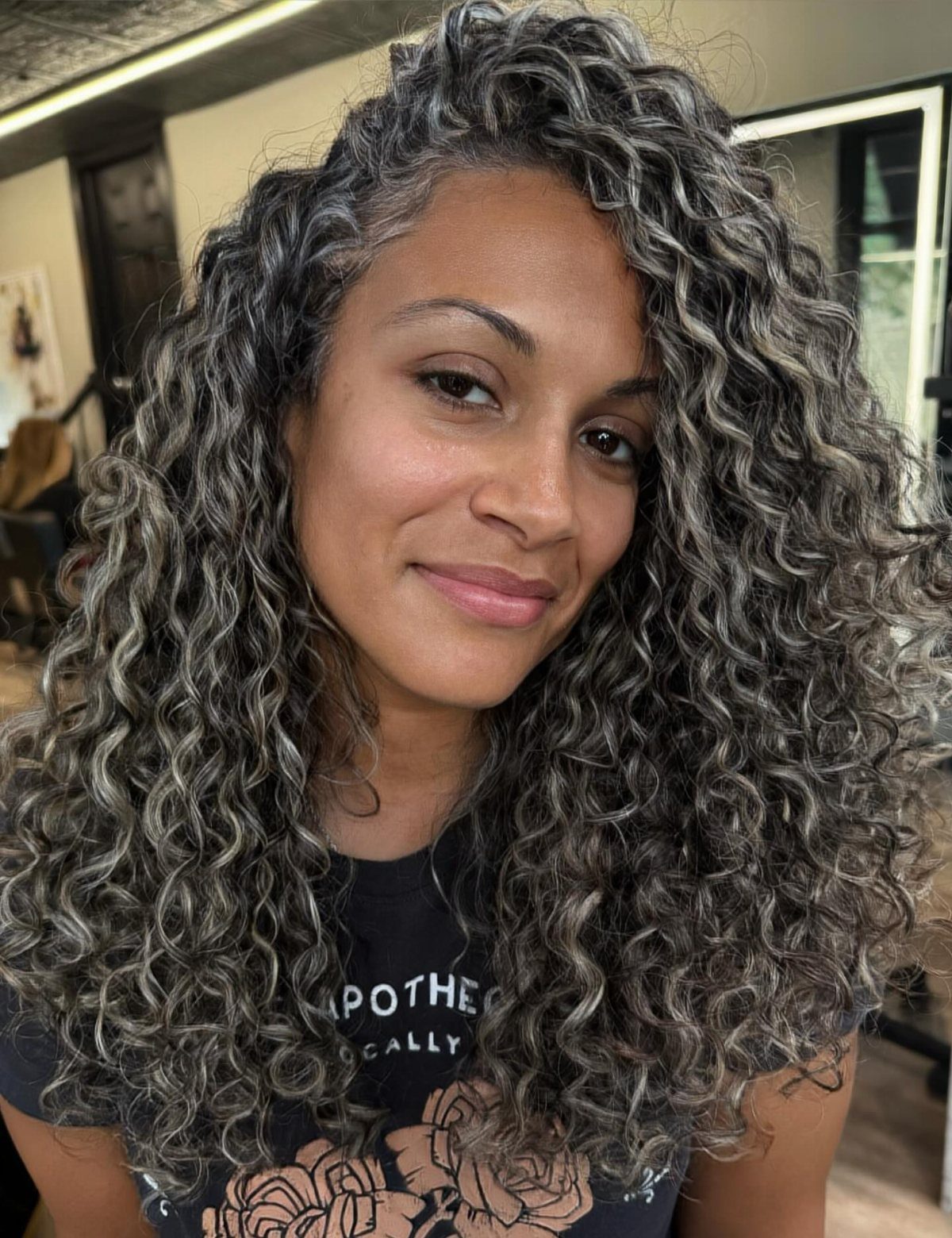 Woman showing long dark curls blended with silver-gray highlights in a salon