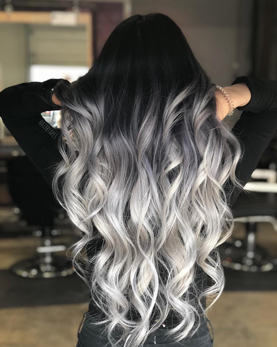 Long dark curls transition through smoky gray to bright silver ends