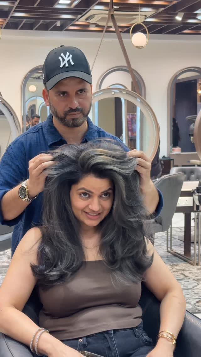 Woman with layered dark hair and gray streaks as a stylist lifts her hair