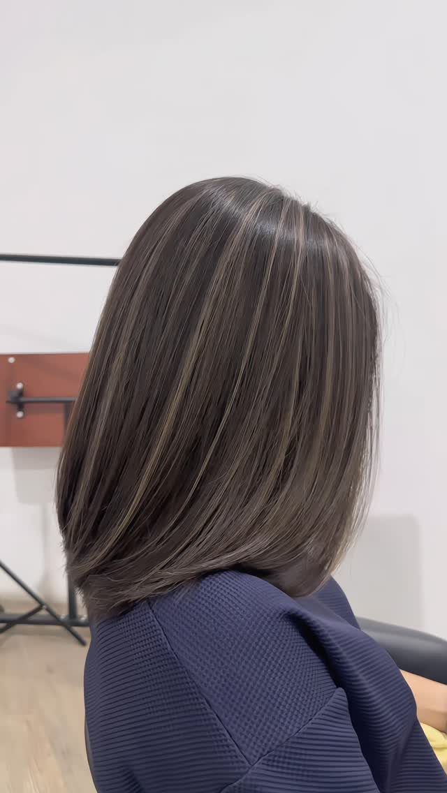 Long dark brown hair with subtle cool gray streaks falls smoothly over a navy top.