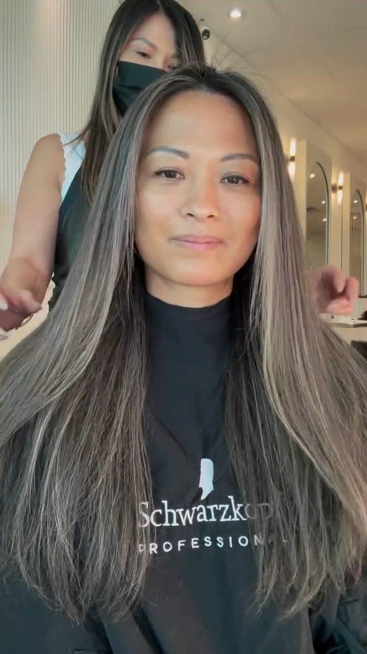 Woman with long dark hair showing blended gray and silver highlights in a salon