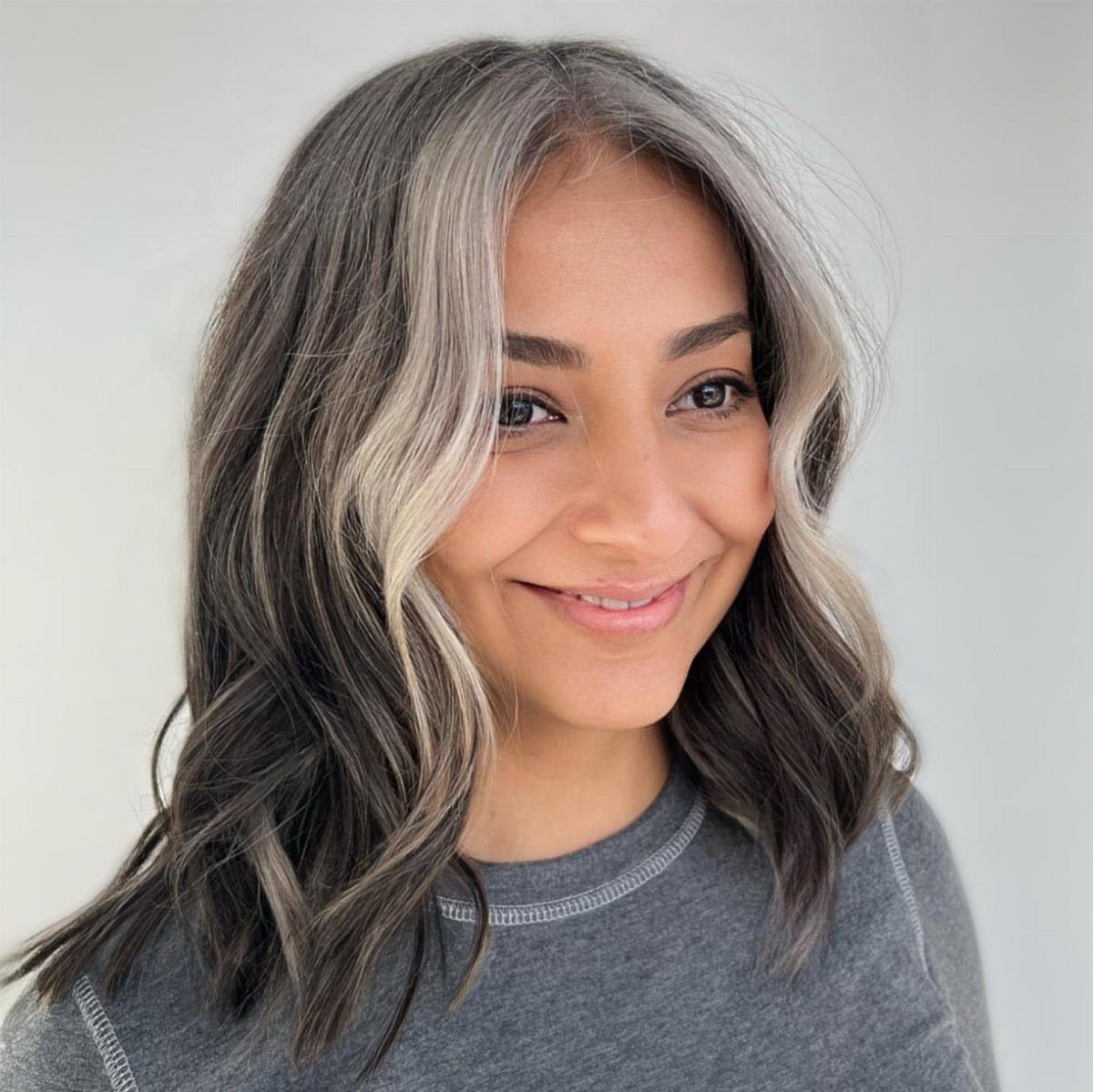 Woman with wavy dark hair and silver highlights framing her face